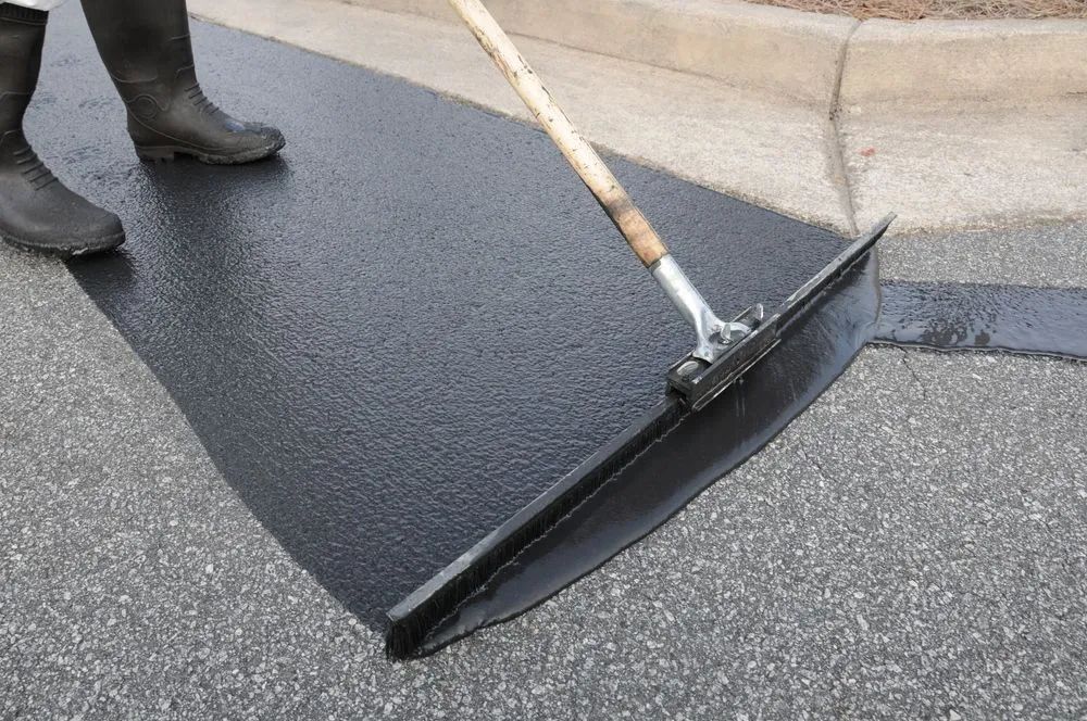 Worker applying sealcoat to an asphalt driveway with a squeegee